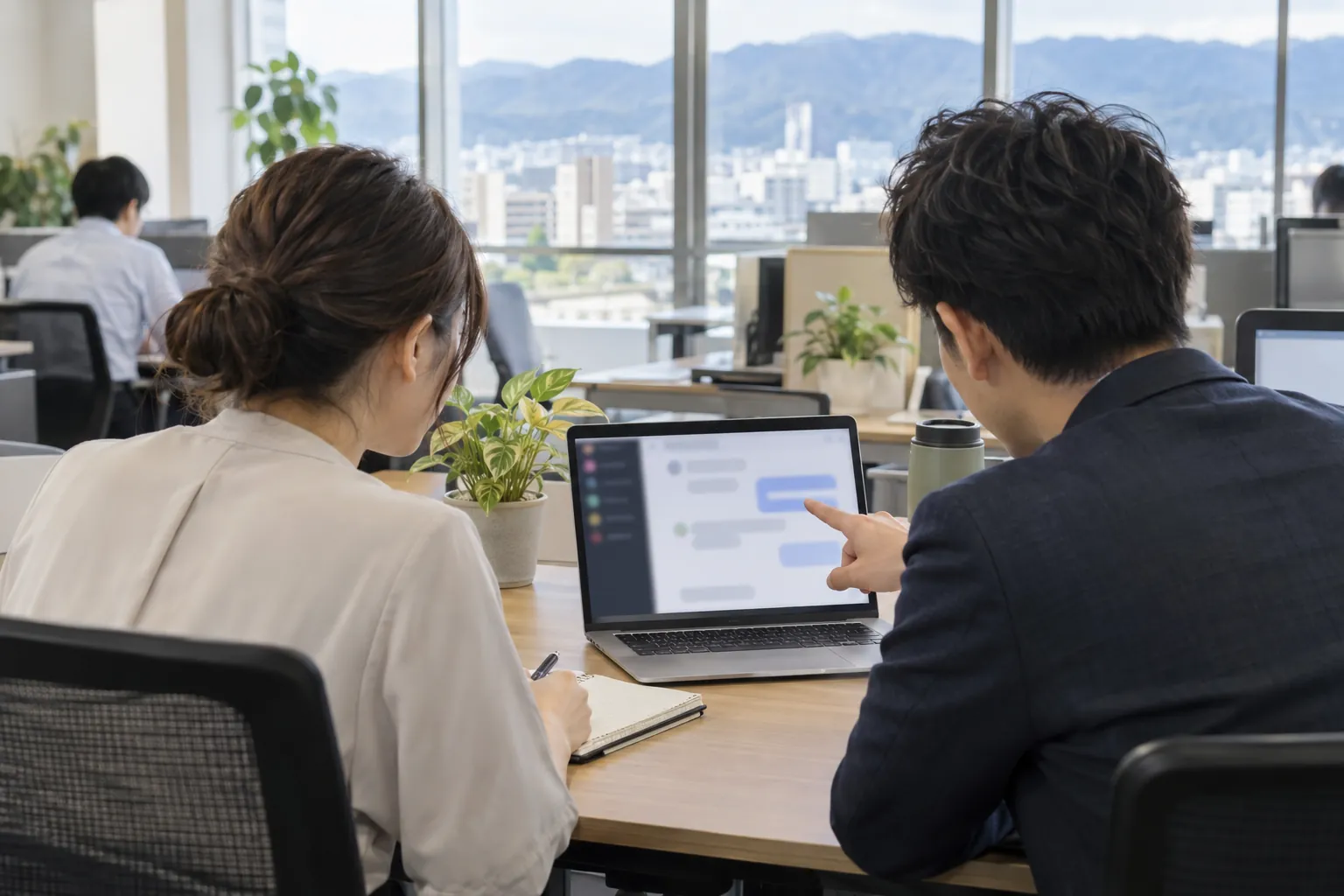 同僚がノートパソコンの画面を指さしながら使い方を教えている