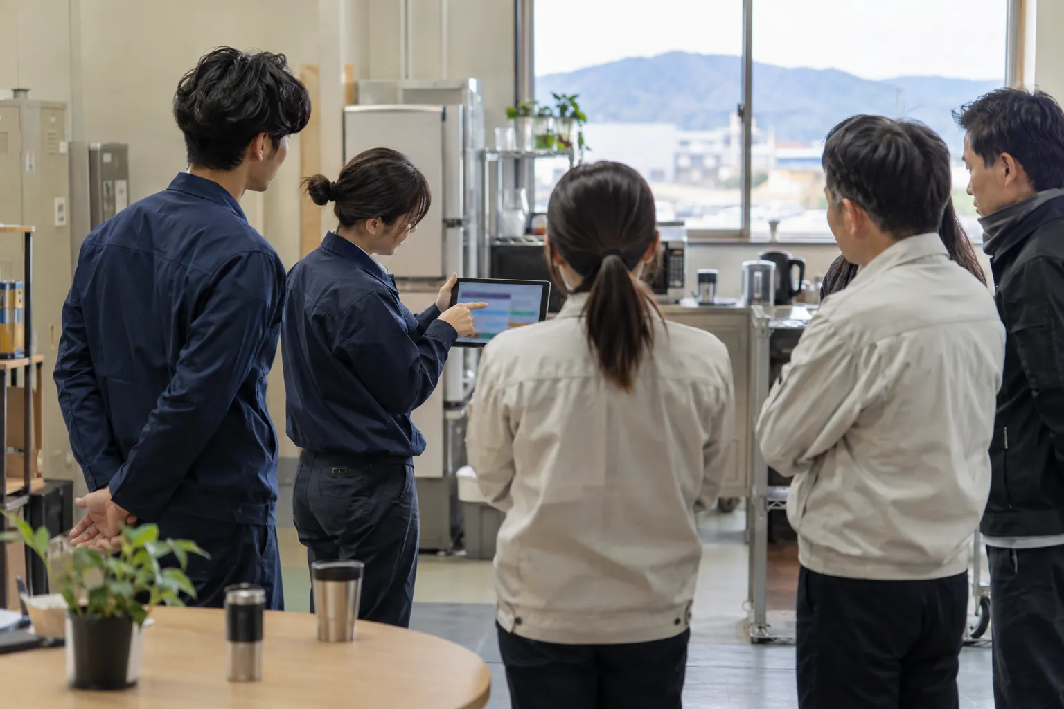 朝礼で社員がタブレットの画面を見せ合っている